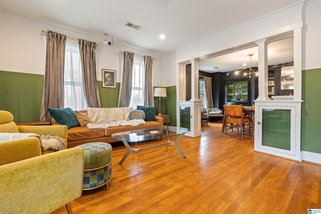 living room featuring decorative columns, hardwood / wood-style floors, a chandelier, and ornamental molding