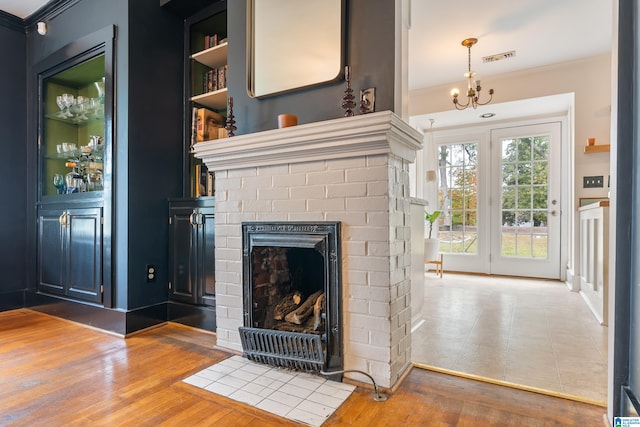 unfurnished living room featuring a brick fireplace, ornamental molding, built in shelves, an inviting chandelier, and hardwood / wood-style floors