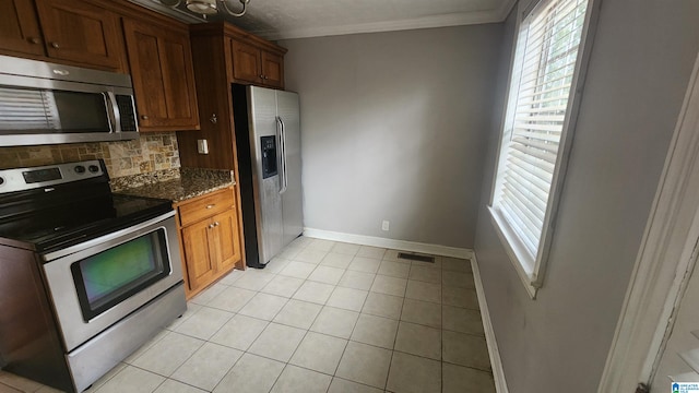 kitchen with stainless steel appliances, tasteful backsplash, dark stone countertops, crown molding, and light tile patterned floors