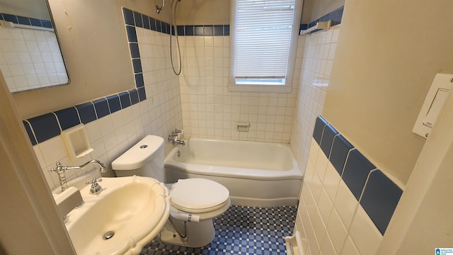 full bathroom with sink, tile patterned floors, tiled shower / bath combo, toilet, and tile walls