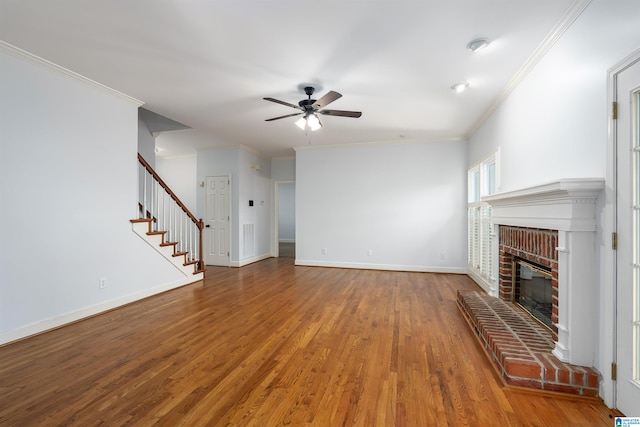 unfurnished living room featuring crown molding, ceiling fan, wood-type flooring, and a brick fireplace