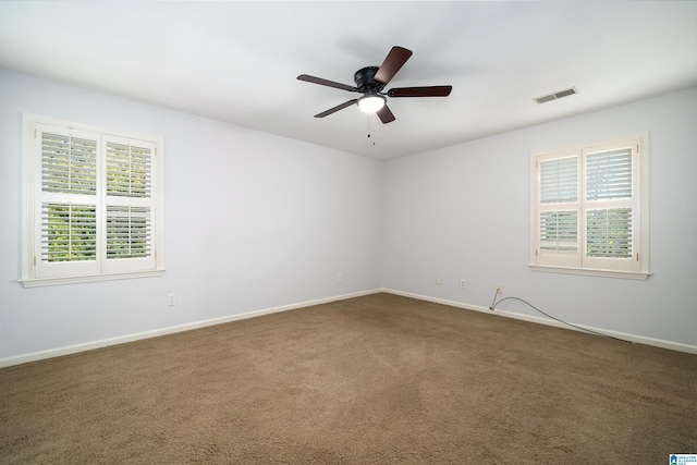 spare room featuring ceiling fan, a healthy amount of sunlight, and dark colored carpet