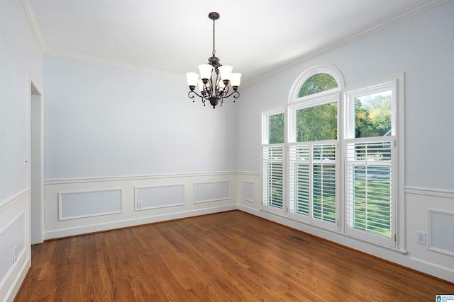 empty room with hardwood / wood-style floors, ornamental molding, and an inviting chandelier