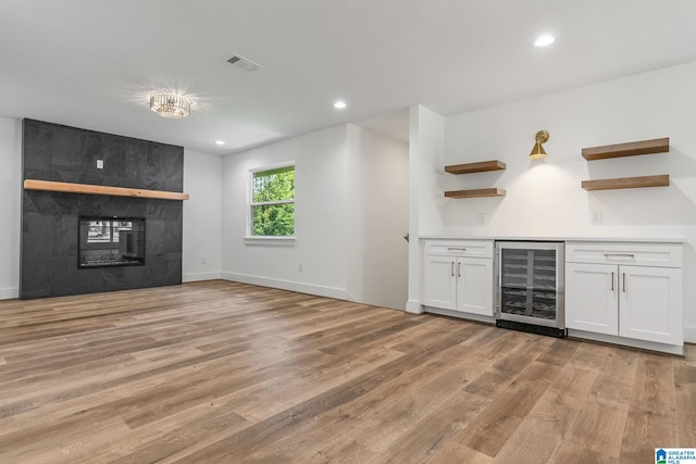 bar with light hardwood / wood-style flooring, white cabinetry, beverage cooler, and a tiled fireplace