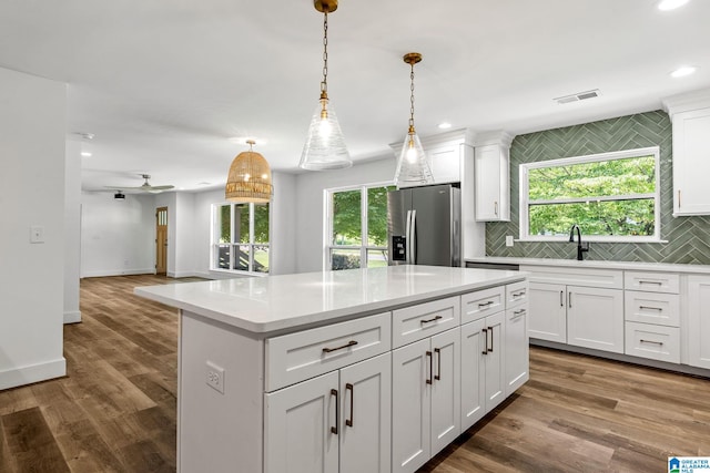 kitchen with stainless steel fridge, white cabinets, and hanging light fixtures