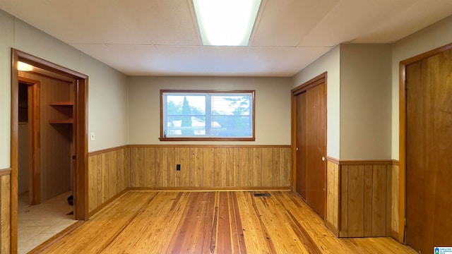 unfurnished bedroom with wooden walls, a closet, and light hardwood / wood-style floors