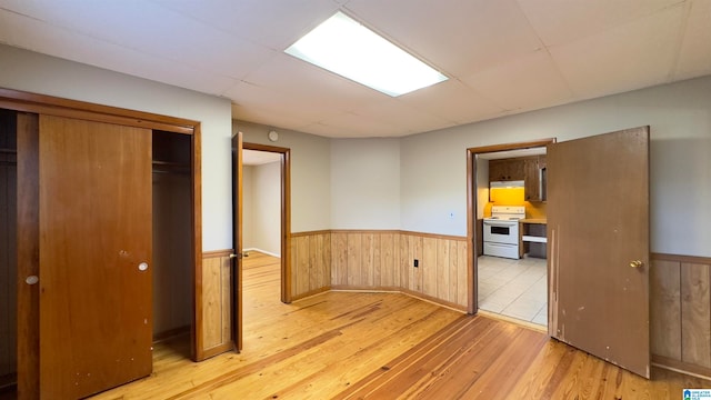 unfurnished bedroom with a closet, wood walls, and light hardwood / wood-style floors