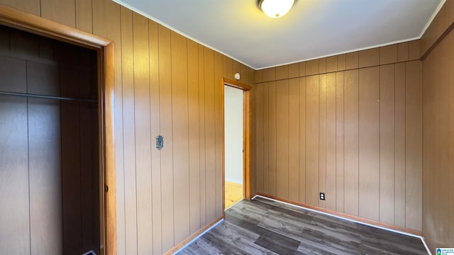 unfurnished bedroom featuring hardwood / wood-style floors, crown molding, a closet, and wooden walls