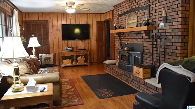 living room with a wood stove, light hardwood / wood-style flooring, ceiling fan, and wood walls