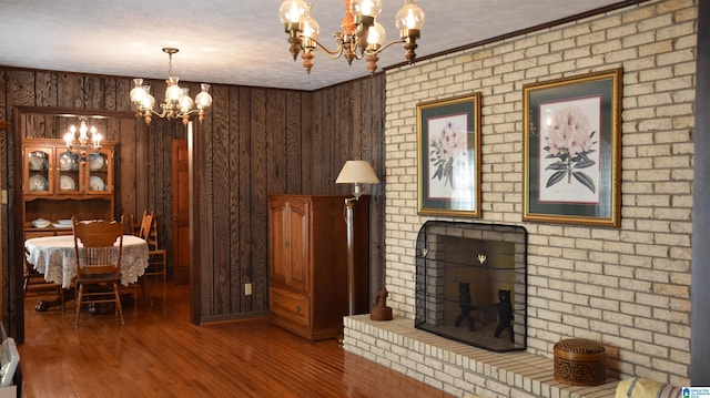 living room featuring wood walls, a chandelier, wood-type flooring, a textured ceiling, and ornamental molding