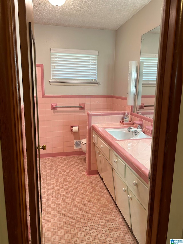 bathroom with a textured ceiling, vanity, toilet, and tile walls