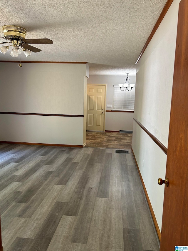 empty room with ceiling fan with notable chandelier, dark wood-type flooring, and a textured ceiling