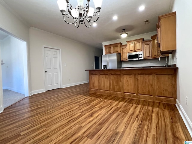 kitchen with kitchen peninsula, hardwood / wood-style flooring, crown molding, and appliances with stainless steel finishes