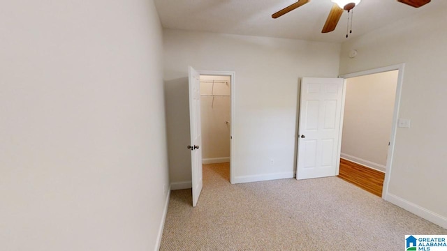 unfurnished bedroom with a walk in closet, ceiling fan, a closet, and light colored carpet