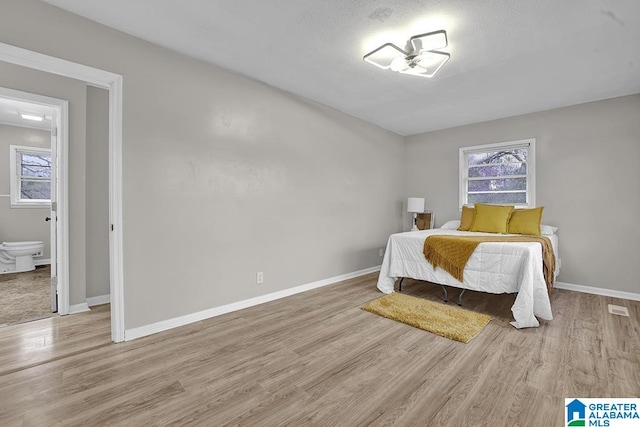 bedroom featuring connected bathroom and light hardwood / wood-style flooring