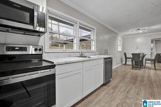 kitchen featuring light wood-type flooring, ornamental molding, stainless steel appliances, sink, and white cabinetry