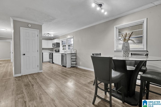 dining area with sink, rail lighting, light hardwood / wood-style floors, a textured ceiling, and ornamental molding