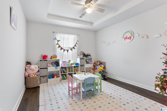 rec room with a tray ceiling, ceiling fan, and dark wood-type flooring