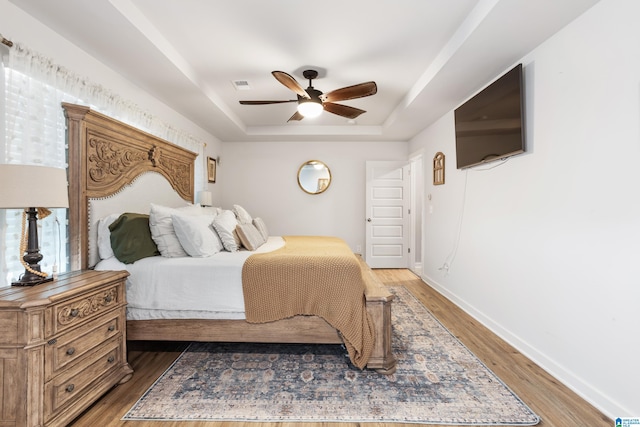 bedroom featuring ceiling fan, a raised ceiling, and dark wood-type flooring