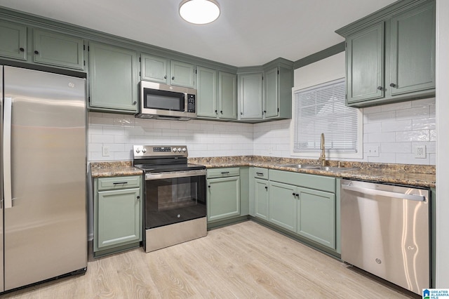 kitchen with backsplash, green cabinets, sink, light hardwood / wood-style floors, and stainless steel appliances