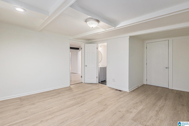 unfurnished bedroom with beamed ceiling, light wood-type flooring, and connected bathroom