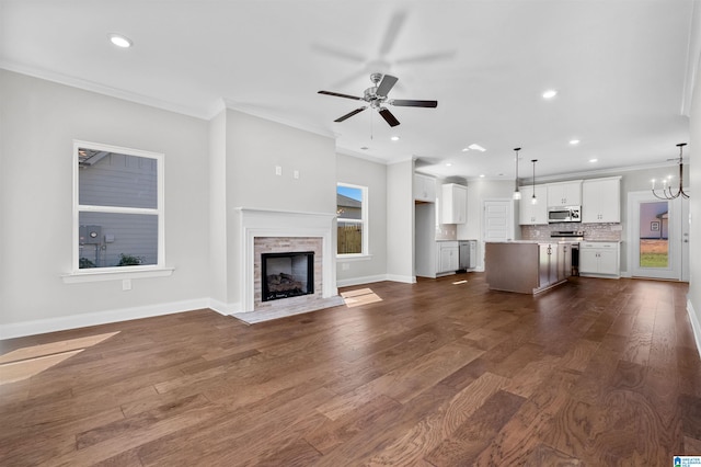 unfurnished living room featuring ornamental molding, ceiling fan with notable chandelier, a stone fireplace, and dark wood-type flooring