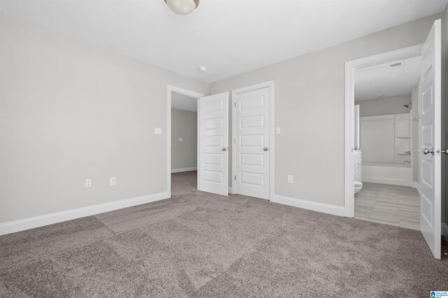 unfurnished bedroom with light carpet, a closet, and ensuite bathroom