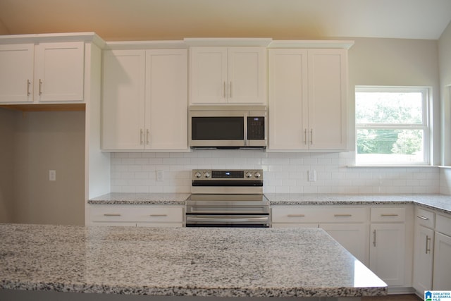 kitchen with tasteful backsplash, white cabinetry, light stone counters, and appliances with stainless steel finishes