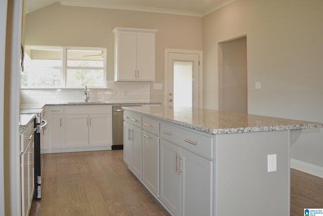 kitchen with sink, a kitchen island, light stone countertops, light hardwood / wood-style floors, and white cabinetry