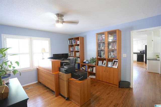 home office with ceiling fan, light hardwood / wood-style floors, and a textured ceiling