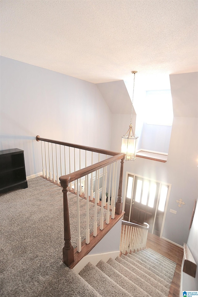 stairway featuring lofted ceiling, wood-type flooring, a wealth of natural light, and a chandelier