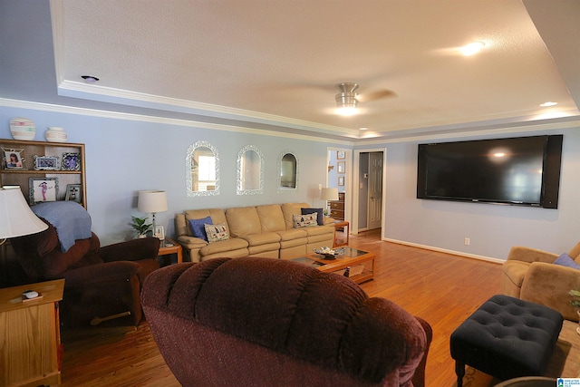 living room with ceiling fan, a raised ceiling, wood-type flooring, and ornamental molding