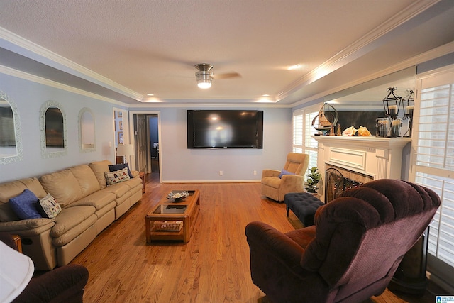 living room with ceiling fan, a raised ceiling, light wood-type flooring, and crown molding