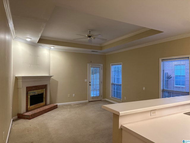 unfurnished living room featuring a tray ceiling, a brick fireplace, ceiling fan, and light colored carpet