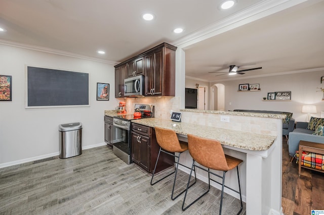 kitchen with kitchen peninsula, a breakfast bar, light hardwood / wood-style flooring, and appliances with stainless steel finishes