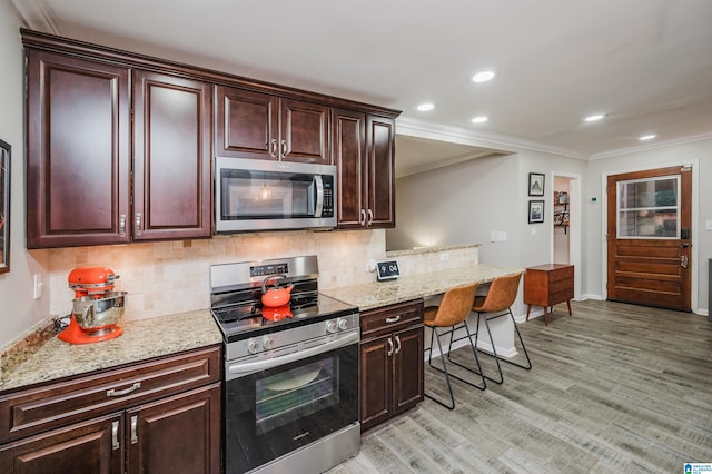 kitchen featuring tasteful backsplash, light hardwood / wood-style floors, a breakfast bar area, appliances with stainless steel finishes, and ornamental molding