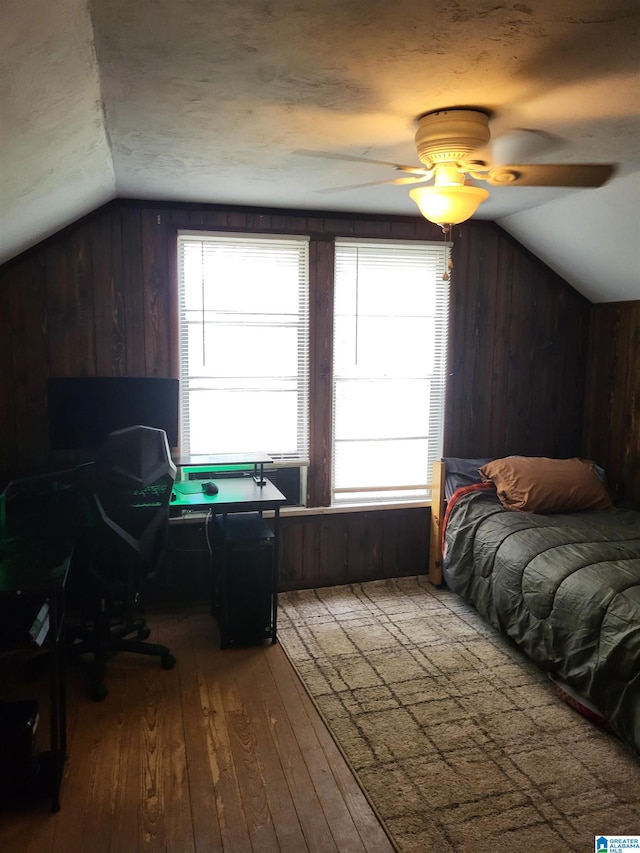 bedroom featuring ceiling fan, wood walls, wood-type flooring, and vaulted ceiling