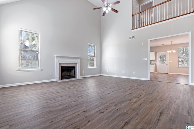 unfurnished living room with a wealth of natural light, a towering ceiling, dark wood-type flooring, and ceiling fan with notable chandelier