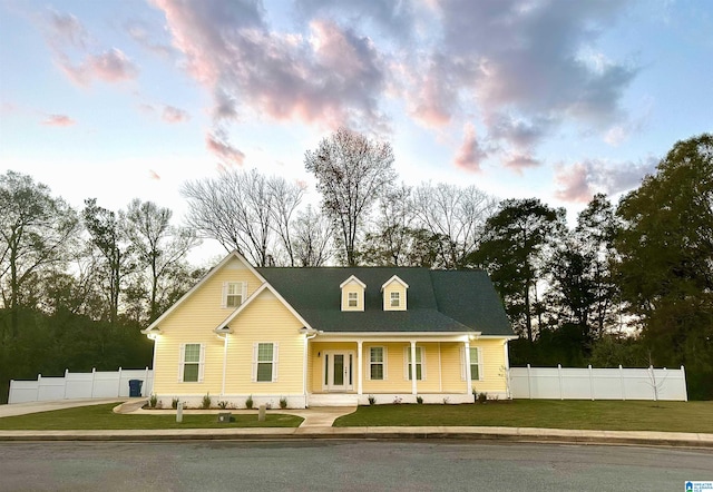 cape cod-style house with a lawn and covered porch