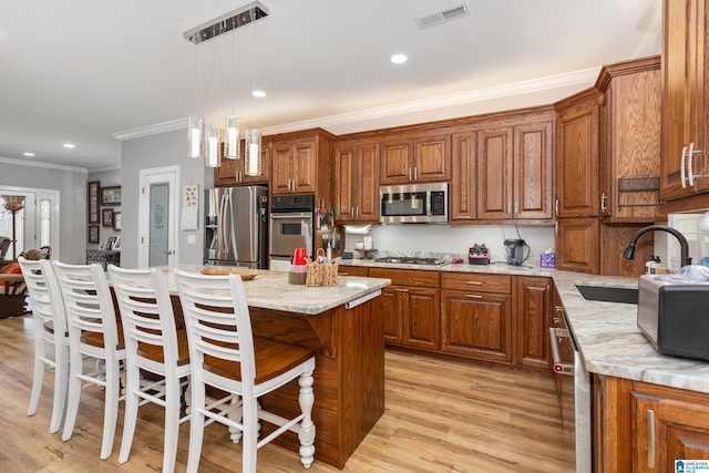 kitchen with hanging light fixtures, light stone counters, appliances with stainless steel finishes, a kitchen island, and light wood-type flooring