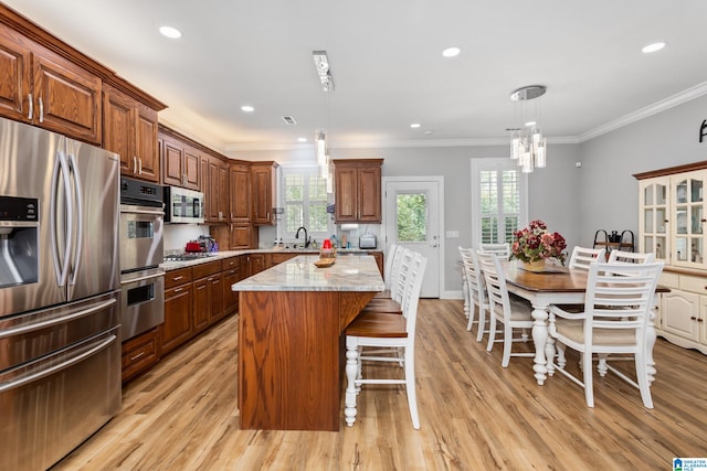 kitchen with hanging light fixtures, a kitchen island, stainless steel appliances, and light hardwood / wood-style floors