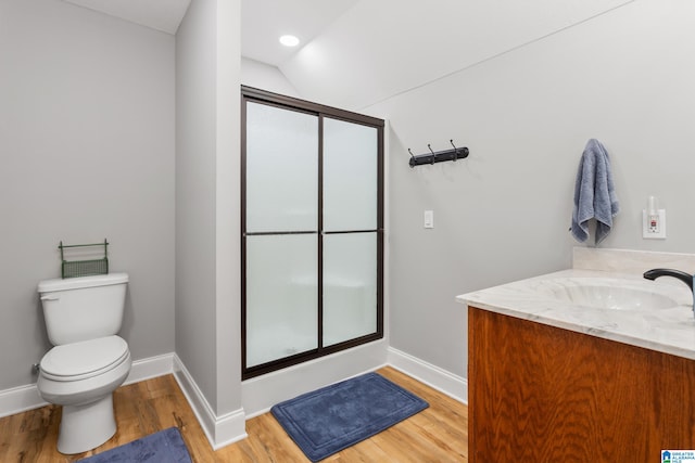 bathroom with hardwood / wood-style floors, vaulted ceiling, toilet, a shower with door, and vanity