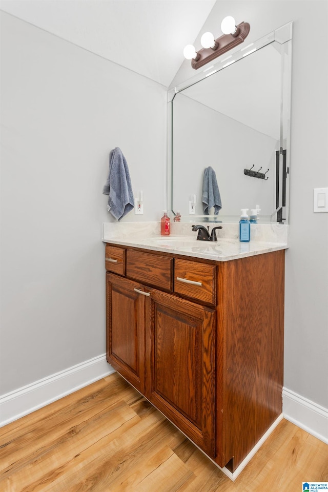 bathroom with hardwood / wood-style floors, vanity, and vaulted ceiling