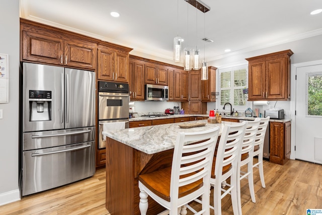 kitchen featuring a breakfast bar, a center island with sink, light wood-type flooring, appliances with stainless steel finishes, and light stone counters