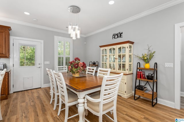 dining area with light wood-type flooring, ornamental molding, and an inviting chandelier