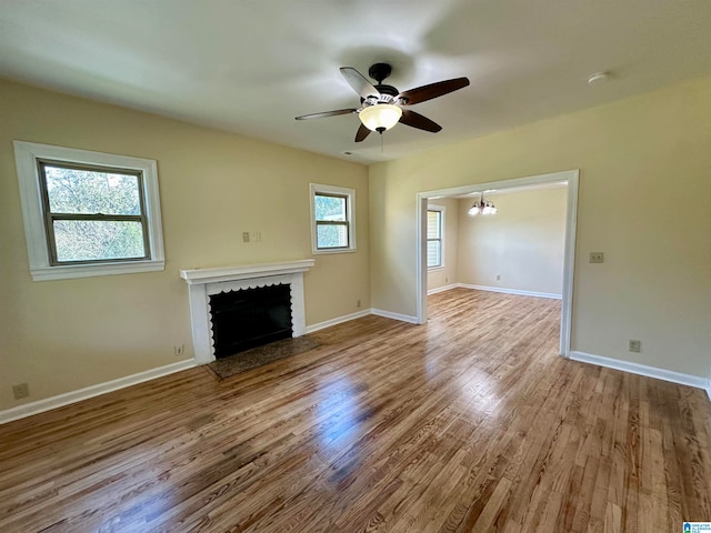 unfurnished living room featuring ceiling fan with notable chandelier and light wood-type flooring