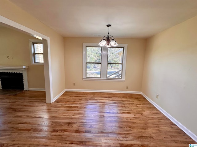 unfurnished dining area with a brick fireplace, light hardwood / wood-style floors, and an inviting chandelier