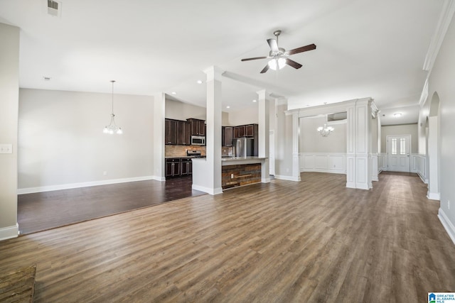 unfurnished living room with ceiling fan with notable chandelier, dark hardwood / wood-style flooring, ornate columns, and ornamental molding