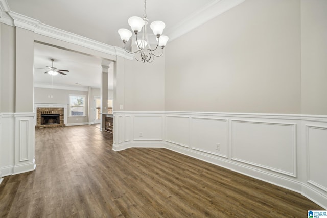 unfurnished dining area featuring ornamental molding, ceiling fan with notable chandelier, ornate columns, and dark wood-type flooring