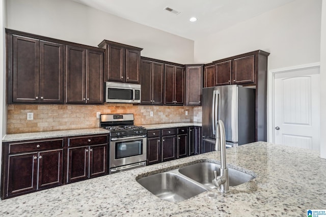 kitchen featuring backsplash, sink, light stone countertops, dark brown cabinetry, and stainless steel appliances